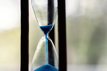 a macro view of a blue sand pouring in the vintage old hourglass