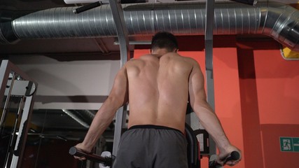 Fototapeta na wymiar Muscular bodybuilder working out in gym doing exercises on parallel bars. Athlitic male naked torso. Athlete is training on parallel bars in the gym