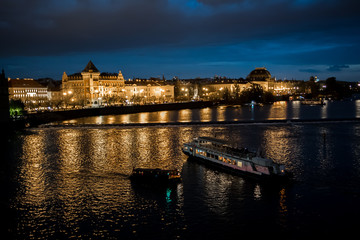 Obraz premium Illuminated Moldova River With Ship And Historic Buildings In The Night In Prague In The Czech Republic