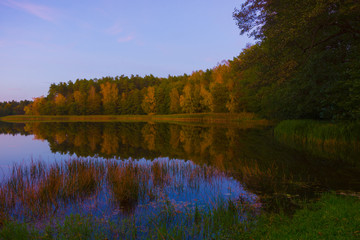 Autumn landscape sunset lake violet sky clouds trees on the shore reflection in the water