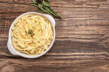 Homemade fettuccine with bechamel sauce in a white plate, rustic wooden table background, soft light - Italian food style