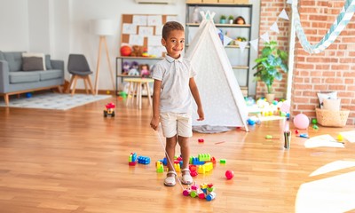 Beautiful african american toddler playing with wooden blocks train toy around lots of toys at kindergarten