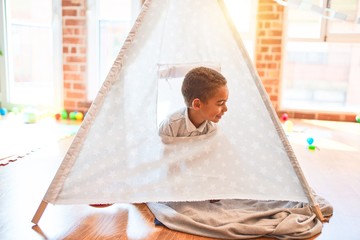 Beautiful african american toddler playing inside tipi smiling at kindergarten