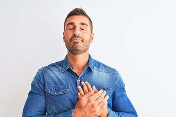 Young handsome man wearing denim jacket standing over isolated background smiling with hands on chest with closed eyes and grateful gesture on face. Health concept.