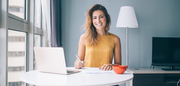 Contented female sitting at table with notebook and cup filling documents