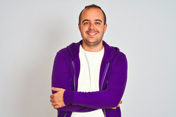 Young man wearing purple sweatshirt standing over isolated white background happy face smiling with crossed arms looking at the camera. Positive person.