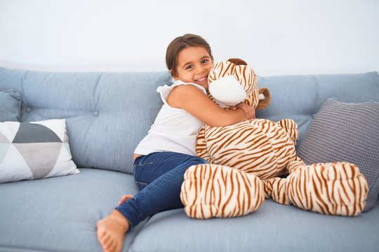 Adorable toddler smiling happy. Sitting on the sofa hugging doll at home