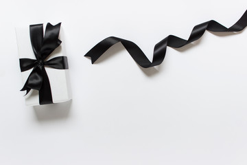Present wrapped in white paper with black satin bow and black shiny twisted satin ribbon on white...