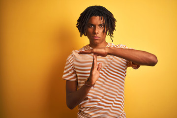 Afro man with dreadlocks wearing striped t-shirt standing over isolated yellow background Doing...