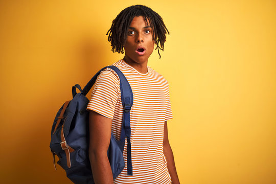 Afro american student man with dreadlocks wearing backpack over isolated yellow background scared in shock with a surprise face, afraid and excited with fear expression