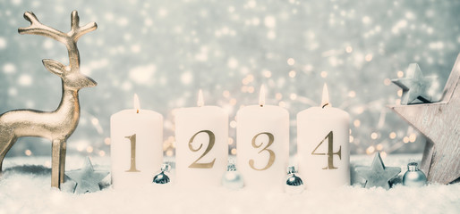 Advent candles 1, 2,3,4 in front of concrete background in the snow with colorful lights and gray trees