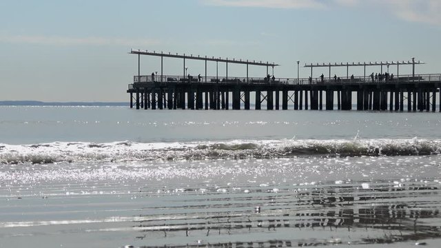 4K. Ultra HD. Images of tourists and locals walking on a pier, with calm waves crashing into the foreground pier. Coney Island Pier, Brooklyn, New York. Travel and nature concept.