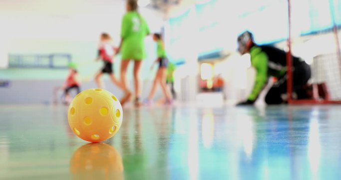 Floorball match of small floorball players. Children play floorball match in indoor hall. Intentionally focused on the ball in the foreground. Players in the background intentionally out of focus.