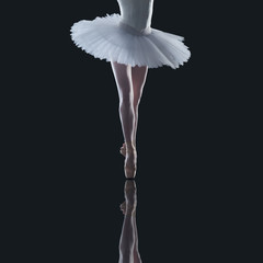 Beautiful ballerina's legs in tutu dress dancing in studio closeup on dark background