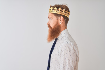 Young redhead irish businessman wearing crown king over isolated white background looking to side,...