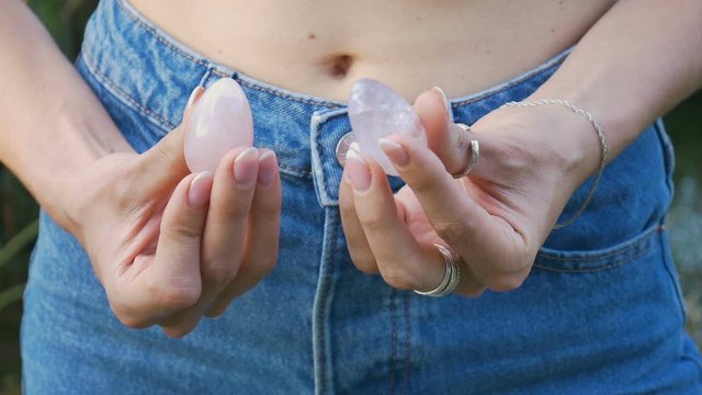 Female hand holding a rose quartz and amethyst crystal yoni eggs. Women's health, unity with nature concepts. Close portrait of an unidentifiable girl in jeans with a bare stomach