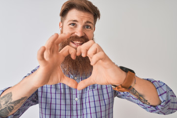 Redhead irish man listening to music using wireless earphones over isolated white background smiling in love showing heart symbol and shape with hands. Romantic concept.
