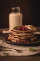 Pancakes with raspberries, banana slices, pomegranate seeds and honey