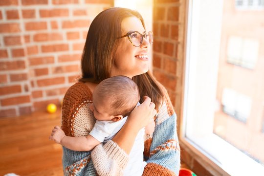 Young beautifull woman and her baby standing at home. Mother holding and hugging newborn