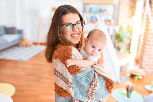 Young beautiful woman and her baby standing at home. Mother holding and hugging newborn