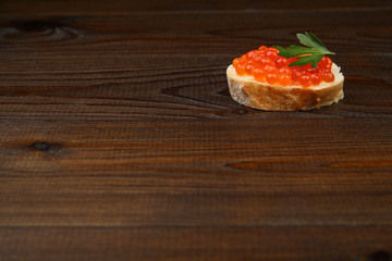 sandwich with red caviar on dark wooden surface with space for text