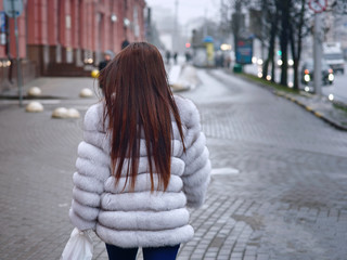 Stylish woman walking down the street on a cold winter in beautiful light blue fur coat. Fashionable girl wearing white fur coat. Female with long hair goes shopping. Shopping concept