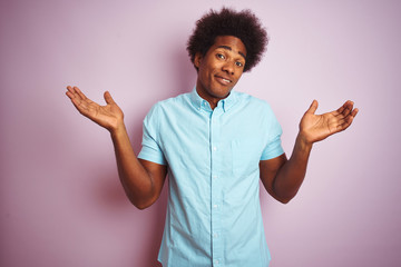 Young american man with afro hair wearing blue shirt standing over isolated pink background...