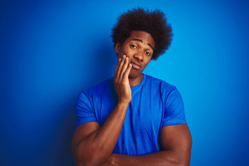 Obraz na płótnie Canvas African american man with afro hair wearing t-shirt standing over isolated blue background thinking looking tired and bored with depression problems with crossed arms.