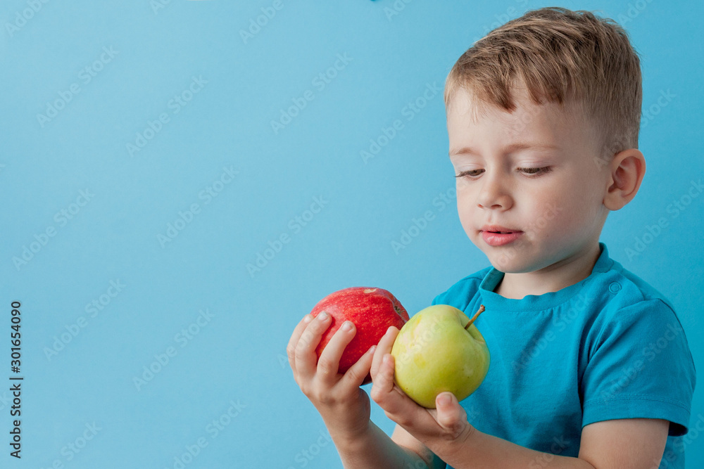 Wall mural Little Boy Holding an Apples in his hands on blue background, diet and exercise for good health concept