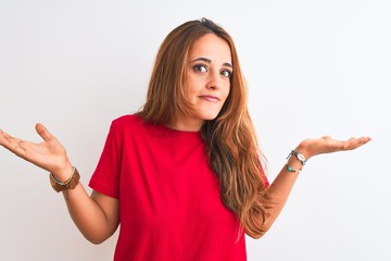 Young redhead woman wearing red casual t-shirt stading over white isolated background clueless and...