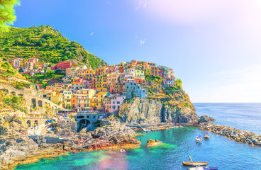 Manarola traditional typical Italian village in National park Cinque Terre, colorful multicolored buildings houses on rock cliff, fishing boats on water, blue sky background, La Spezia, Liguria, Italy - Powered by Adobe