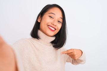 Young chinese woman wearing turtleneck sweater make selfie over isolated white background with surprise face pointing finger to himself