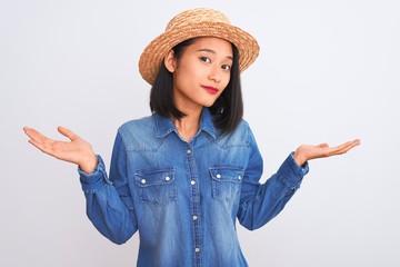 Young beautiful chinese woman wearing denim shirt and hat over isolated white background clueless...