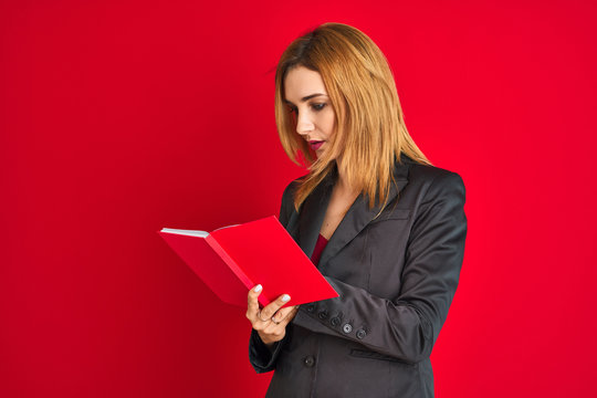 Young beautiful redhead businesswoman wearing suit reading book
