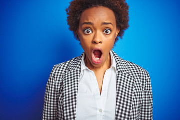 African american business executive woman over isolated blue background afraid and shocked with surprise expression, fear and excited face.