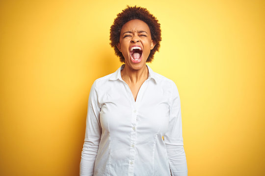 African american business woman over isolated yellow background angry and mad screaming frustrated and furious, shouting with anger. Rage and aggressive concept.