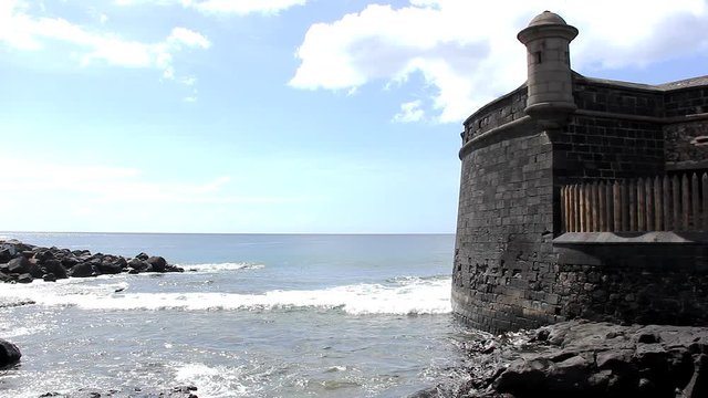 San Juan Bautista castle by the sea in Tenerife, Canary Islands. Small waves  reaching shore by black castle on sunnny day