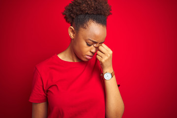 Fototapeta na wymiar Young beautiful african american woman with afro hair over isolated red background tired rubbing nose and eyes feeling fatigue and headache. Stress and frustration concept.