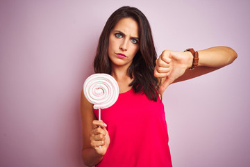 Young beautiful woman eating sweet candy over pink isolated background with angry face, negative sign showing dislike with thumbs down, rejection concept
