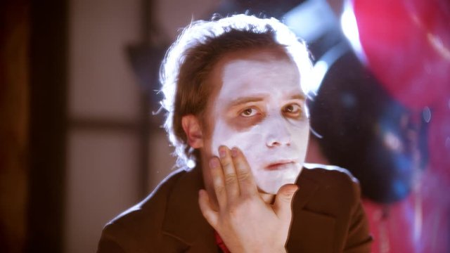 A man smearing white paint on his face in front of the mirror in the dressing room
