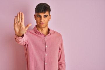 Young indian man wearing elegant shirt standing over isolated pink background doing stop sing with palm of the hand. Warning expression with negative and serious gesture on the face.