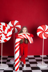 New Year 2020! Christmas, holidays and childhood concept. Merry Christmas, happy holidays! Little girl with a big christmas candy cane on an isolated red background. Huge Christmas Candies. sweets