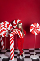 New Year 2020! Christmas, holidays and childhood concept. Merry Christmas, happy holidays! Little girl with a big christmas candy cane on an isolated red background. Huge Christmas Candies. sweets