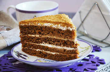 A piece of honey cake with cream on a table in a plate with a cup of coffee
