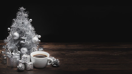 A christmas (new year) white cup of coffee and silver christmas tree on wooden table at black background with copy space for your text
