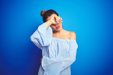 Young beautiful woman wearing bun hairstyle over blue isolated background covering eyes with arm, looking serious and sad. Sightless, hiding and rejection concept