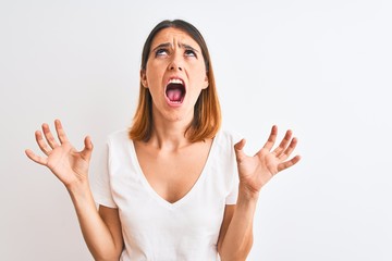 Beautiful redhead woman wearing casual white t-shirt over isolated background crazy and mad shouting and yelling with aggressive expression and arms raised. Frustration concept.