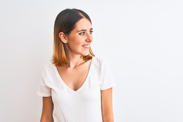 Beautiful redhead woman wearing casual white t-shirt over isolated background looking away to side with smile on face, natural expression. Laughing confident.