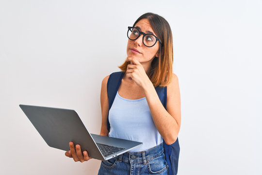 Beautiful redhead student woman wearing a backpack and using laptop serious face thinking about question, very confused idea