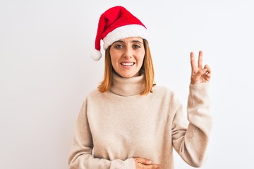 Beautiful redhead woman wearing christmas hat over isolated background smiling swearing with hand...